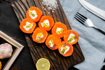 Salmon rolls with cream cheese and pistachios on a wooden cutting board. Luxury catering. Top view.