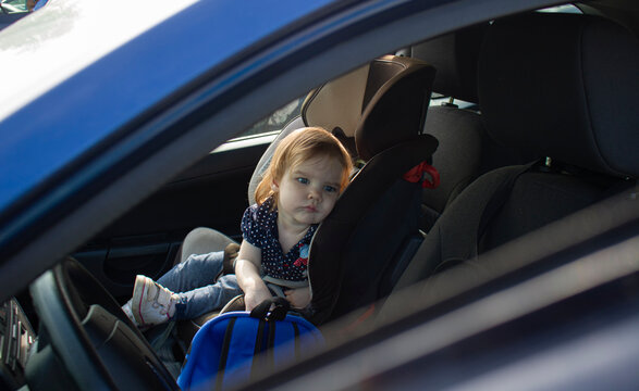 Sad Little Child Girl Alone In The Car Waiting For The Parent Strapped In A Child Car Seat. It Is Dangerous To Leave Children In The Car In Hot Weather.