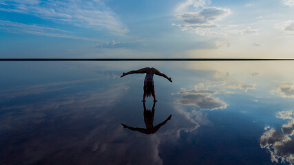Beautiful flexible slender girl balances handstand in mirror reflection of sea and sky