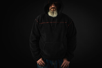 young, serious man with a long beard, a man in a black jacket with a hood on his head. On a dark, emotional background. place for inscription. Low key