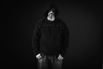 young, serious man with a long beard, a man in a black jacket with a hood on his head. On a dark, emotional background. place for inscription. Low key