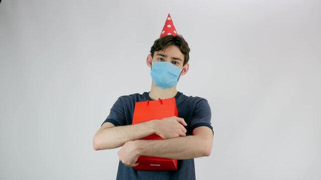 The guy with the beard in mask and cap. Birthday, protective mask. post messages or various advertising banners. Guy with a gift. copy space. Covid 19. 4K resolution