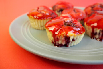 six gluten-free muffins with rice flour cherries and drizzled cherry and red syrup stand on a gray plate on a red background side view . homemade cakes