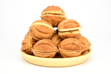 Walnut shaped cakes filled with condensed milk on a wooden plate isolated on a white background