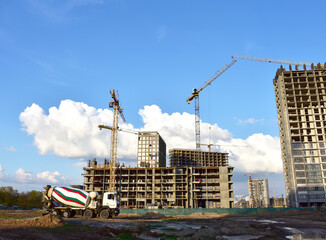 Heavy mixer concrete truck for to be loaded concrete at a construction site. Tower crane lifting a concrete bucket for pouring concrete through and formworks. Constructing new building.