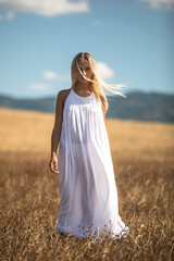 Fototapeta na wymiar Ragazza bionda con vestito bianco su campo di grano e cielo azzuro