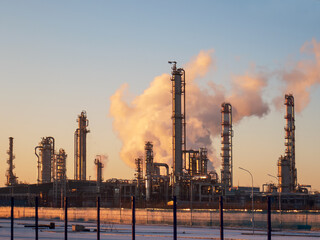 Oil refinery behind the fence in the evening at sunset