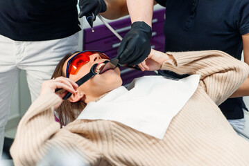 Dentist with assistant takes an intraoral photo of female patient's teeth which sitting in the dental chair.