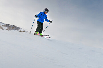 Fototapeta na wymiar child with helmet and blue jacket is skiing fast on the slopes