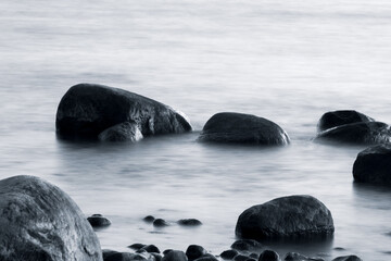 Long exposure of sea and rocks. Boulders sticking out from smooth wavy sea. Tranquil scene.