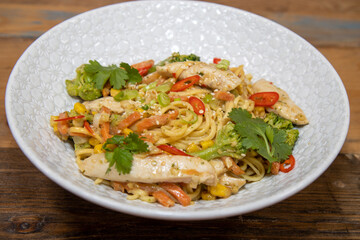 A top down view of a plate of delicious stir-fry ginger and peanut chicken noodle in a white bowl in a kitchen