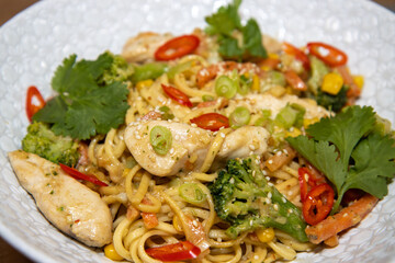 A top down view of a plate of delicious stir-fry ginger and peanut chicken noodle in a white bowl in a kitchen