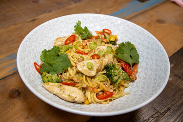 A top down view of a plate of delicious stir-fry ginger and peanut chicken noodle in a white bowl in a kitchen