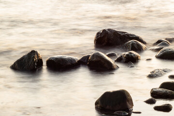 Long exposure of sea and rocks. Boulders sticking out from smooth wavy sea. Tranquil scene.