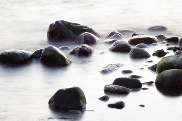 Long exposure of sea and rocks. Boulders sticking out from smooth wavy sea. Tranquil scene.