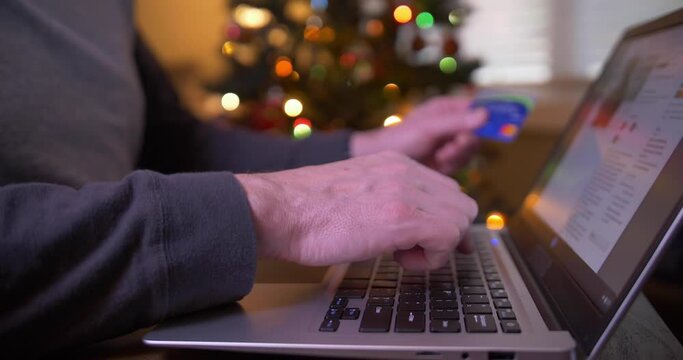 A closeup shallow depth of field view of a man online shopping with a laptop PC next to a Christmas tree.  	