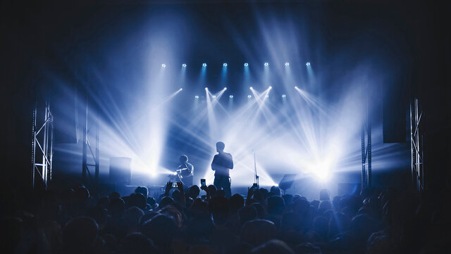 silhouette of the soloist standinf in a fog in the rays of light. concert crowd in front of bright stage lights. Dark background, smoke, concert  spotlights