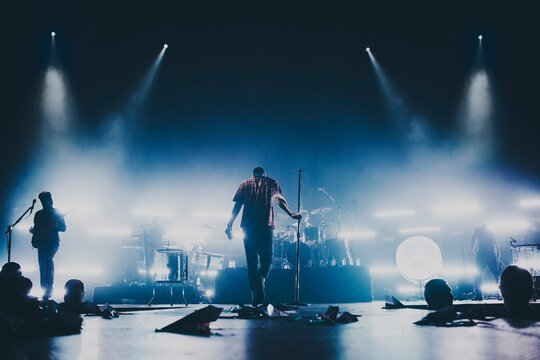 Music Band Silhouette Perform On A Concert Stage.  Dark Background, Smoke, Concert  Spotlights, Singer Holds A Microphone Stand.