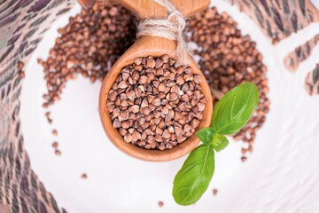 Raw buckwheat groats and basil leaf in wooden spoon