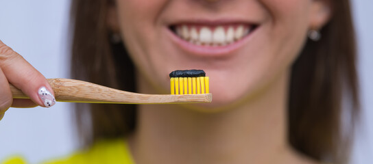 Close up of eco friendly bamboo toothbrush with black charcoal toothpaste. Happy woman brushing...
