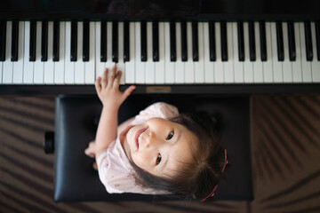 Asian toddler girl look up with smiling while playing piano, exploring music instrument, performance, early childhood music education, leisure activity, top view © ztony1971
