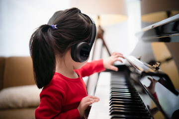 Toddler 3 years old girl explore piano, listen to music on headphone and playing piano, new normal, learning online, e-learning, home learning, musician, early childhood music, child activity