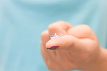 Contact lens on human hand on blue background. Selective focus. Close up