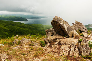 Bay of the sea and large rocks from the hilltop of the mountainous coast, summer landscape and seascape in cloudy cloudy weather.