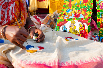 Young Bengali female artist painting Pattachitra or Patachitra on white cloth - traditional,...