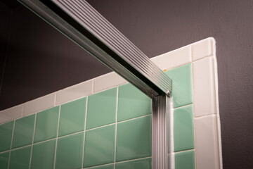 View of sliding shower door frame, in retro colored and styled home bathroom setting.