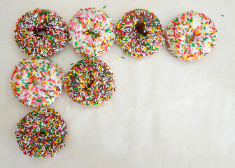 Flat lay view of many frosted donuts, chocolate and vanilla with candy sprinkles arranged in a row top and side on a parchment paper