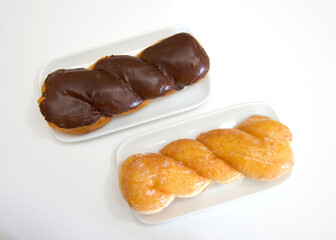 Top view flat lay of one glazed twist donut and one chocolate covered glazed twist on a rectangular off white porcelain plates, on parchment paper.