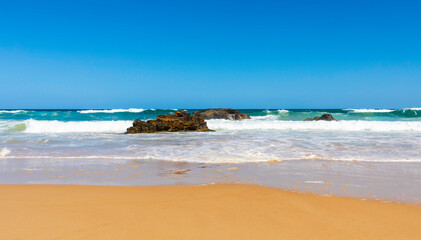 Blue sky and waves  breaking on small rock formations and smooth sandy beach on Mid North Coast,NSW, Australia