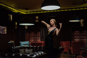 A graceful ballerina in a black dress posing in a restaurant. Beautiful elegant woman dancing in a dark room © Михаил Решетников