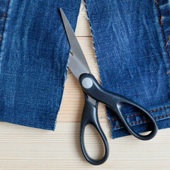 Scissors pieces of cut denim. Wood background.