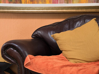 Closeup of a brown leather chair, an orange cloth and a yellow pillow
