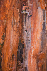 A strong man climbs a beautiful orange rock.