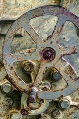 A metal control wheel on an old, decrepit piece of machinery is showing some rust and age.