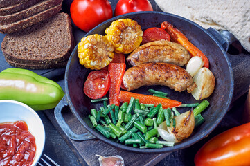 Homemade fried sausages with vegetables in a frying pan