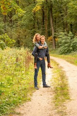 Fototapeta premium Attractive young couple, man carries woman on his back in the woods. They stand still on a sandy forest path
