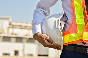 Professional Engineer holding white hard hat on site construction background