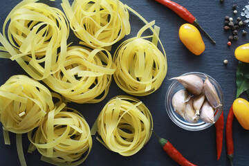 Pasta on the table with spices and vegetables. Noodles with vegetables for cooking on a black stone background.