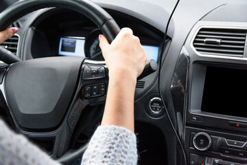 Fototapeta premium Young woman in blue sweater is sitting in the car behind the wheel.. Female driver is driving the car in cloudy day. Woman hands on the steering wheel