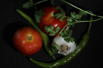 Green chilly, Garlic, Tomato, Onion and Curry leaf are isolated on black background. Ingredients concept. Hot and spicy green chillies and fresh ripe tomato, Onion on black background.