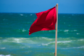 Red danger warning lifeguard safety flag waving in windy weather on the blue ocean coast landscape during summer in Hallandale Beach, Florida as hazardous storms approach 