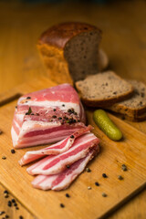 Raw bacon on a wooden plate wish shot glass, pickle and black bred. Homemade bacon on wooden board
