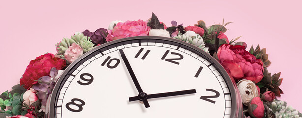 Part of big analogue plain wall clock in full bloom flowers on candy pink background. Close up floral banner, time management concept. Daylight saving time. Spring or wedding. Womens day picnic