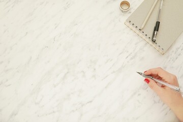 Office desk and woman hand top view, blogger work space flatly with marble background, place for text or design, notebook, pencil, pen.