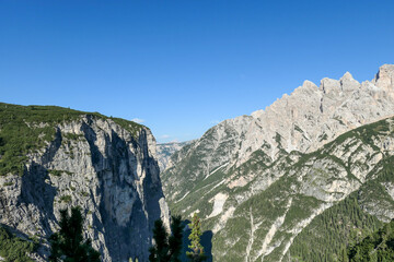 A close up view on the steep slopes of Italian Dolomites. The slopes are stony, partially covered with small plants. A few tree branches in the view. Sunny and bright day. Shap and high mountains