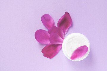 Top view of white cream for body, hand and face skin care with peony extract and magenta floral petals